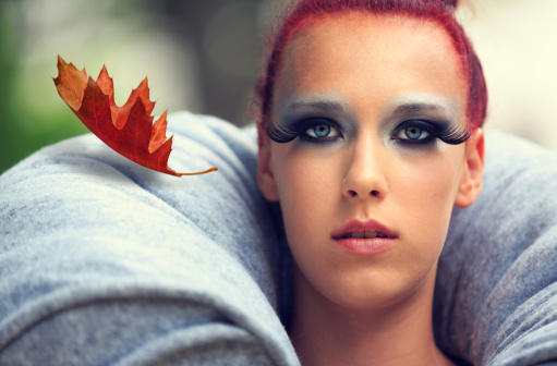 Red-haired woman with blue eyes with a dry autumn leaf falling by her side.
