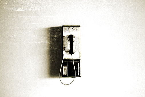 A grungy image of a pay phone and shadow on a blank white wall.