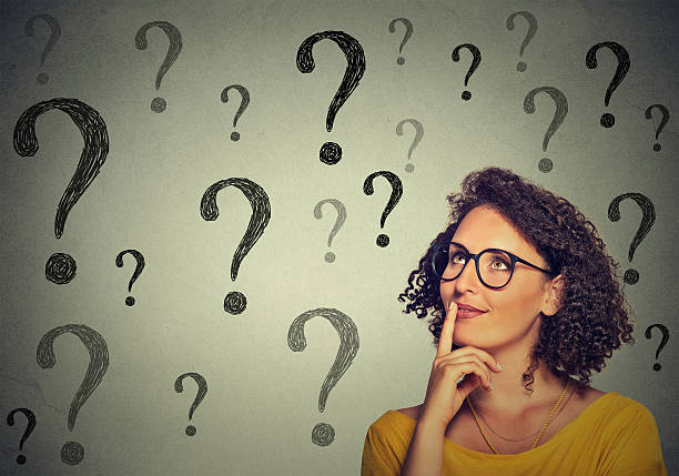 Thinking woman in glasses looking up at many question marks