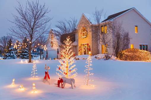 Festive family home with Christmas, holiday decorations, covered in snow. The cold of the winter outdoors only makes the home look warm, friendly and inviting.