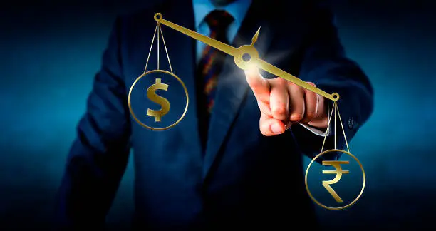 Indian rupee currency symbol is outbalancing the US or Canadian dollar sign on a golden weight scale. A trader is touching the center of the slanting virtual balance. Metaphor for the forex market.