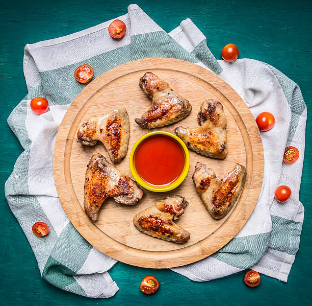 Grilled chicken wings spicy chili sauce  cutting board  top view Grilled chicken wings with spicy chili sauce on a cutting board on a striped napkin cherry tomatoes on rustiс wooden background  top view close up buffalo iowa stock pictures, royalty-free photos & images