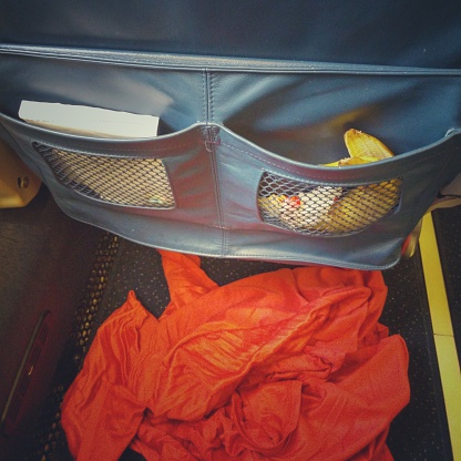 Messy passenger left dirty airplane passenger seat pocket behind with banana peel, trash, blanket on floor.