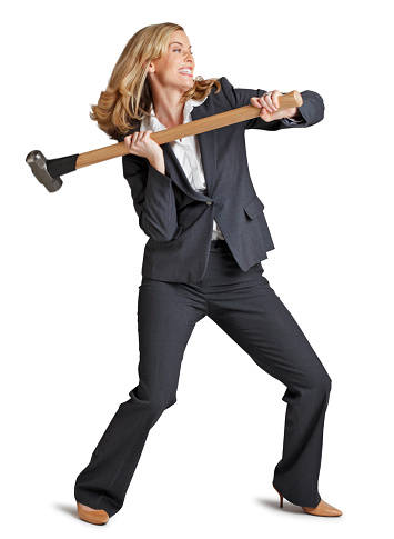 A businesswoman swinging a sledgehammer isolated on a white background. She is grasping sledge hammer with both hands while using all the strength she has to swing it.