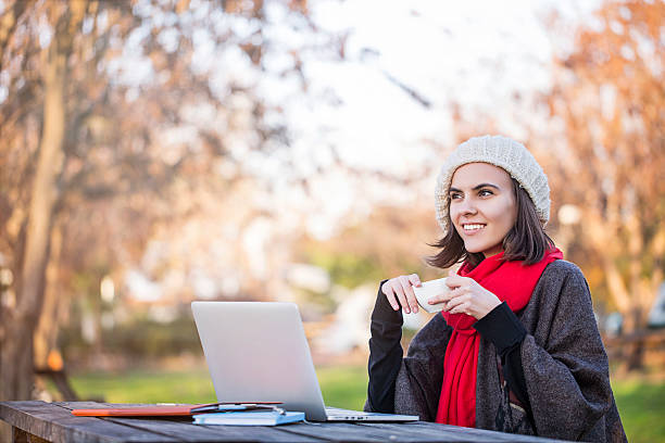 istock Woman using a laptop in a park while drinking coffee 503058906