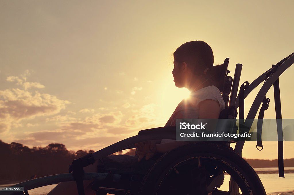 Teenage Girl In Wheelchair Teenage girl with cerebral palsy sits in a wheel chair watching the sunset by a river. Cerebral Palsy Stock Photo