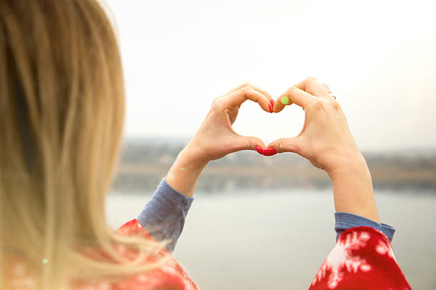 istock Young woman by the lake making heart shape finger frame 503082416