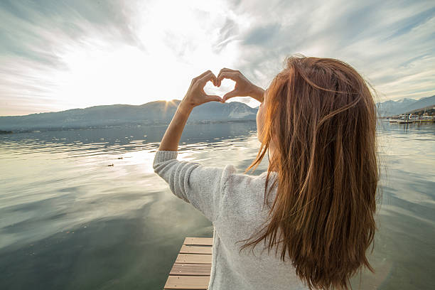 istock Woman on pier above lake makes heart shape finger frame 503083786