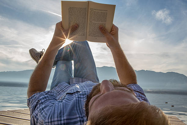 istock One man lies on jetty above lake, reads a book 503083986