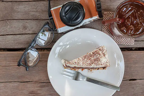 Banoffe cake, a glass of lemontea, eyeglass and camera on the wood in the morning