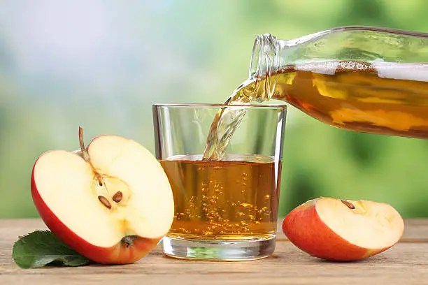 Apple juice pouring from red apples fruits in summer into a glass