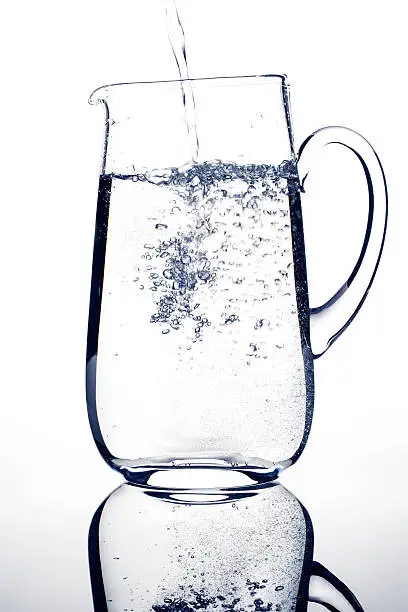 Pouring sparkling water into a carafe - back lit