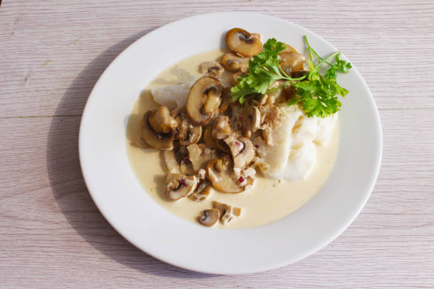 Top down view of plate of fish in creamy white wine and mushroom sauce. 
