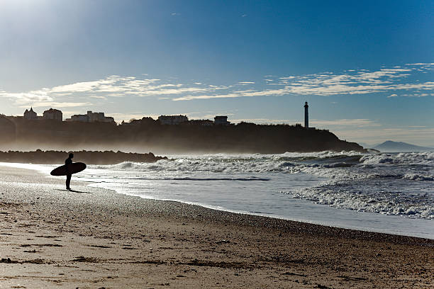 Surfer silhouette in front of the Ocean Surfer silhouette at Chambre d'Amour beach with Biarritz lighthouse behind. french basque country photos stock pictures, royalty-free photos & images
