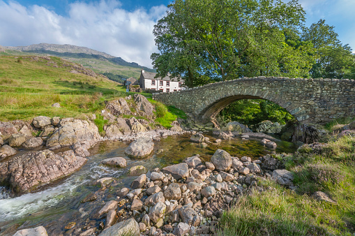 Clear mountain river under an old stone bridge against a white washed cottage and mountain backdrop