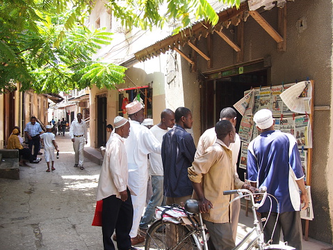 Stone Town, Zanzibar, Tanzania - November 27, 2015: A group of local men crowd round a shop to read the newspapers in Zanzibar's capital. Nobody actually buys the paper, they just all read it from a distance. 