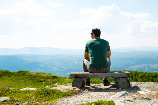 Lonely man sitting on mountain top, smiling.