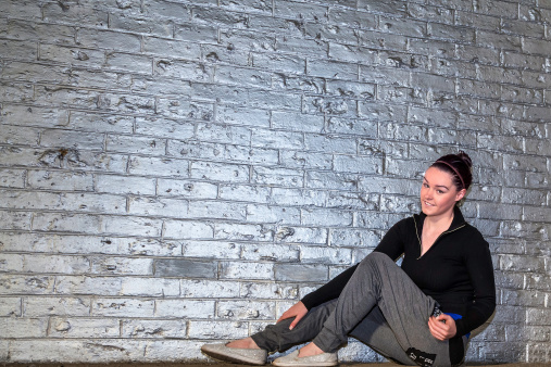 Young woman sitting down against a silver brick wall.