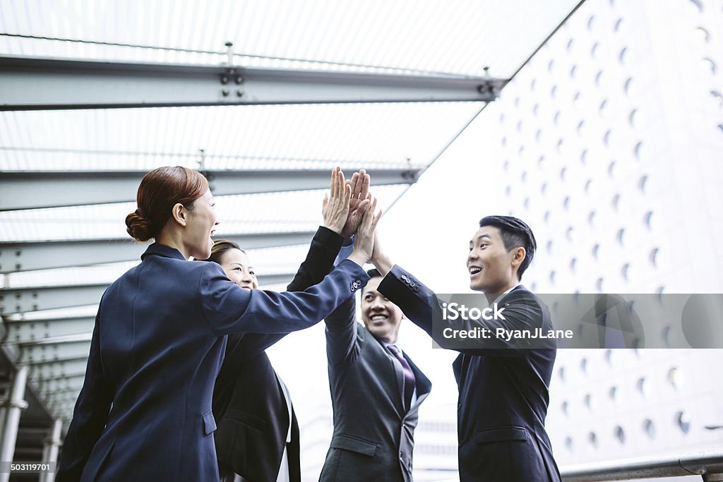 Asian Business Team High Five A group Chinese business men and woman laugh and while giving each other a high five in celebration of a success. Urban city shot in Hong Kong. Horizontal image. Asia Stock Photo