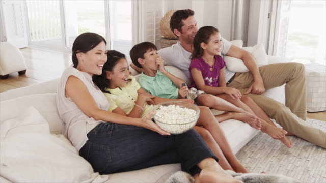 Family sitting on sofa eating popcorn while watching television