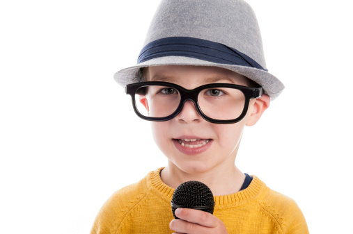 Geeky toddler boy talking in a microphone,  wearing big glasses and a hat. Studio shot isolated on white.