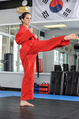 Female martial artist executing a roundhouse kick in her training hall.