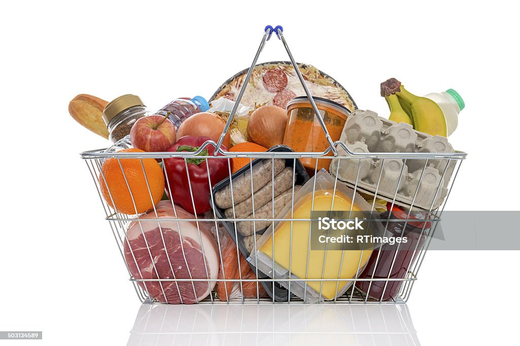 Shopping basket full of groceries isolated on white. Studio shot of a shopping basket full of food including fresh fruit, vegetables, meat, pizza and dairy products. Isolated on a white background. Food Stock Photo