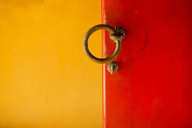 Doorhandles of an open, red door against a yellow background