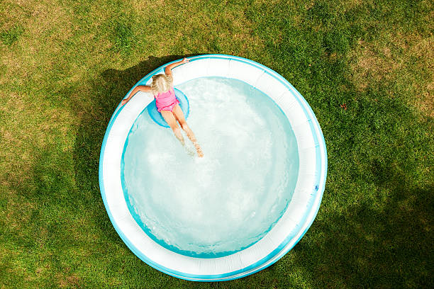 Girl in Inflatable Swimming Pool, Summer Day on Dried Grass A six year old girl is relaxing in an inflatable swimming pool on a hot Summer day. She is sitting on a blue inner tube, the grass is becoming dry and brown and the shadow in the lower right is from a tree. plastic paddling pool stock pictures, royalty-free photos & images