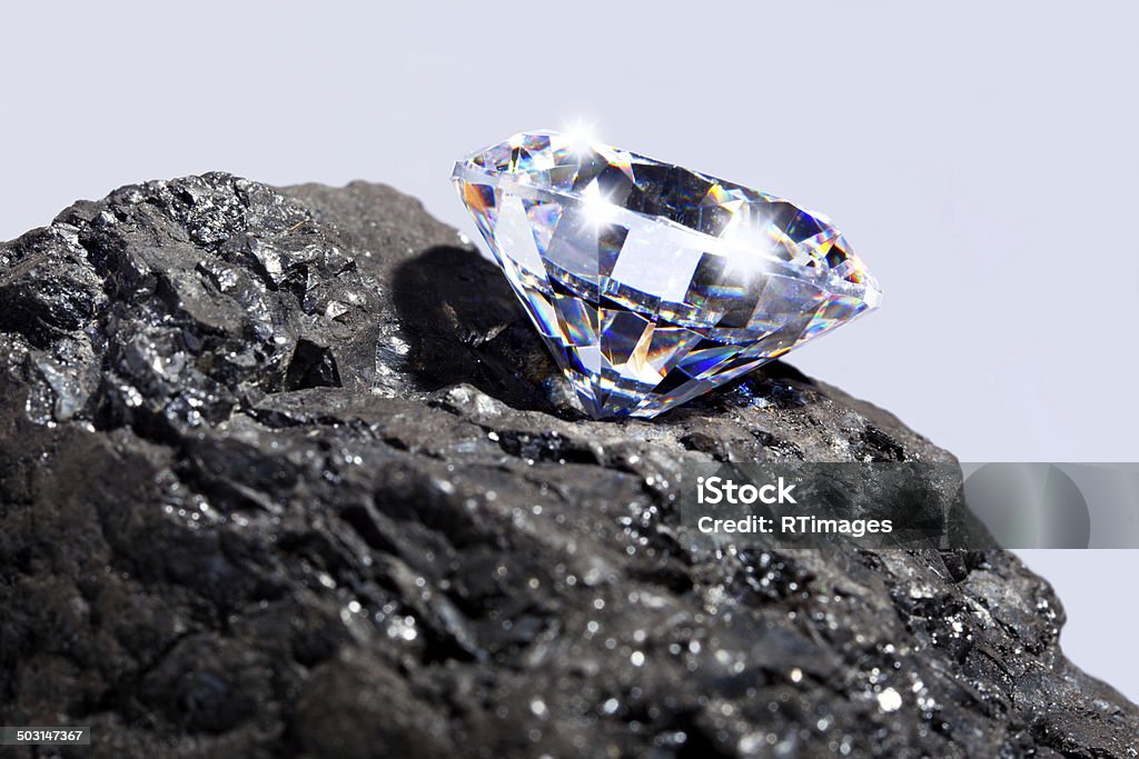 Diamond and Coal Photo of a single cut diamond on a piece of coal against a plain background. Close-up Stock Photo