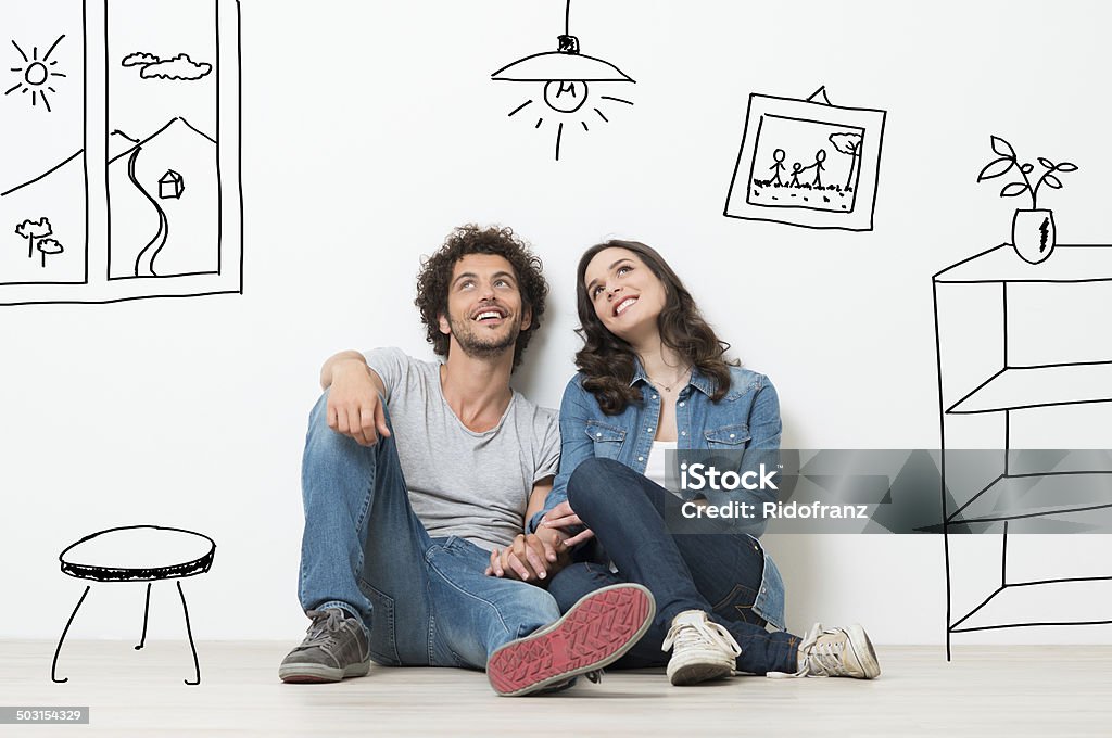 Happy Couple Dream New Home Portrait Of Happy Young Couple Sitting On Floor Looking Up While Dreaming Their New Home And Furnishing Couple - Relationship Stock Photo