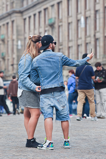 Amsterdam, The Netherlands - August 26, 2014: Fashionable dressed Caucasian couple takes selfie on Amsterdam Dam Square. the city is a source of inspiration for fashionable people. there are many ways to soak up Amsterdam's fashionable vibe.