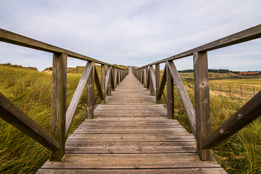 A wooden pathway crossing a dunes area by the sea.