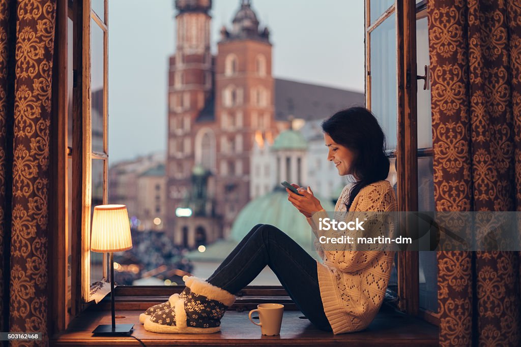 Woman texting on the window sill Happy woman using smartphone at home Krakow Stock Photo