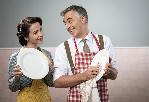 Smiling vintage couple in apron dish washing together