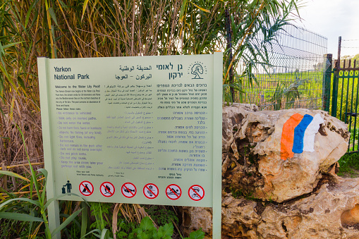 Yarkon National Park, Israel - December 19, 2015: Sign of the Water Lily Pool in the Yarkon National Park. On the sign there is information and rules of conduct that must exist in the area. Near it painted a Israel hiking trail marker. The picture was taken during a trip to the area.