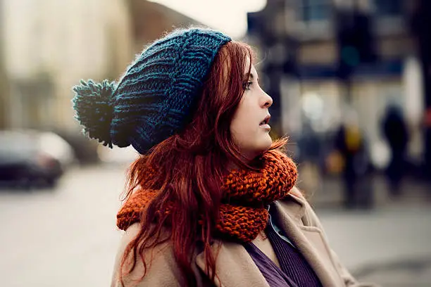 Young Woman in winter clothing with long red hair looking to the side, outdoors in a UK town.