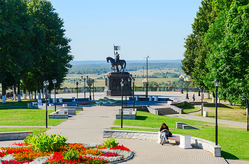 Vladimir, Russia - August 21, 2015: An unknown girl sits on a bench in a park named after Pushkin near the monument to Prince Vladimir and holy hierarch Feodor, Vladimir, Golden Ring of Russia