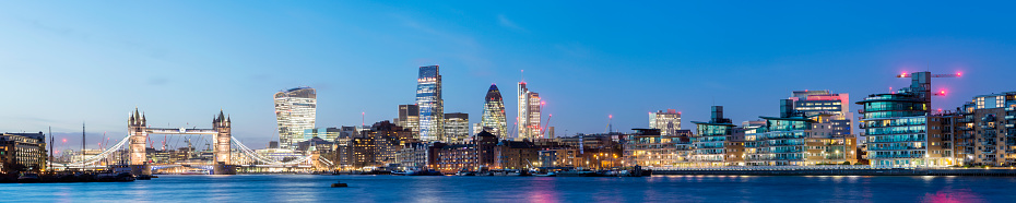 Panoramic view of Tower Bridge and the downtown city skyline at twilight on the River Thames, London, England.