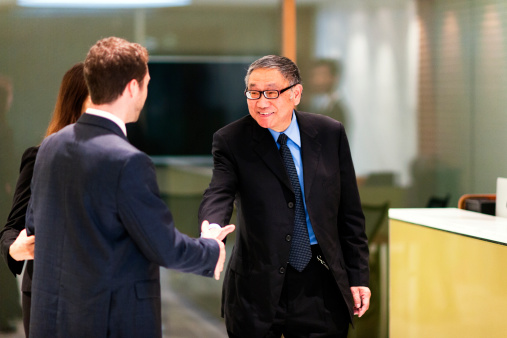 Cropped shot of two businesspeople shaking hands while colleagues are blurred in the background