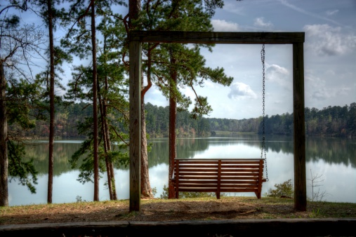 A summer or spring lake scene of an inviting chair.