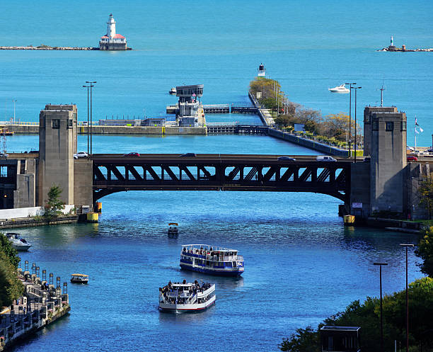 Tour boats at the mouth of the Chicago River in  downtown Chicago.  Lakeshore Drive Bridge, Harbor Lock, lighthouse and Lake Michigan. Distant people on boats.