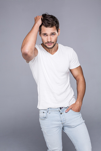 Handsome man touching his hair. Fashion model posing in white t-shirt looking at camera and touching his hair