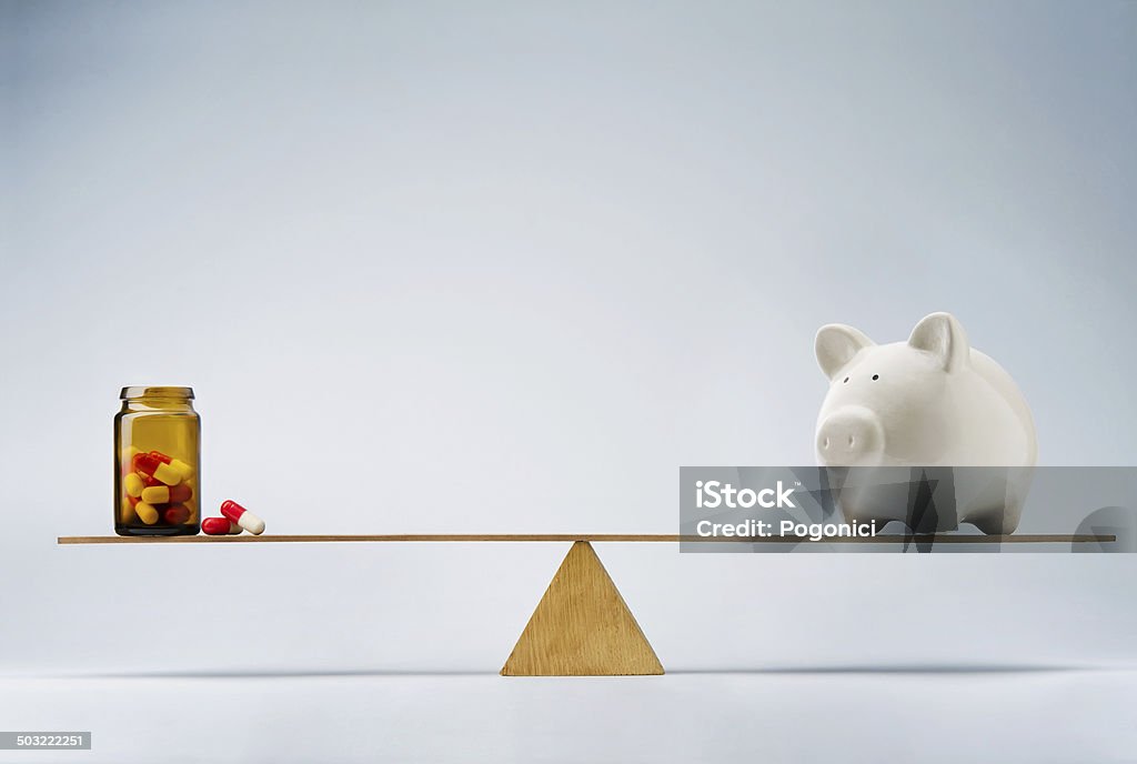 Medical costs or insurance fund concept Piggy bank balancing on seesaw over a bottle of pills Currency Stock Photo