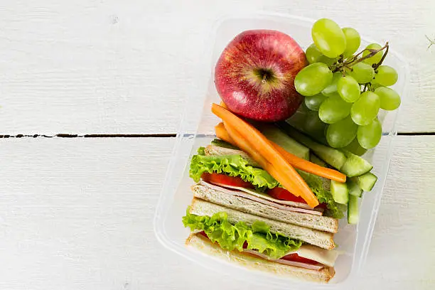 Lunchbox with sandwich, vegetables, fruit on white background. Top view