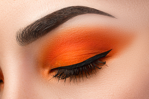 Close-up of woman eye with beautiful orange smokey eyes with black arrow makeup. Modern fashion make-up.