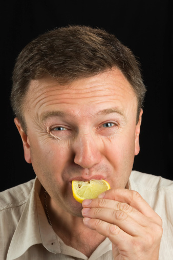 A man eats a lemon on a black background