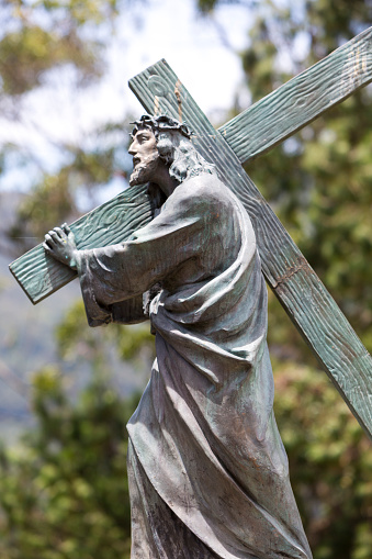 Antique statue of Christ carrying the Christian cross part of the Basilica of the Senor de Monserrate with blue sky, designed by architect Arturo Jaramillo Concha in 1925. Located on the Cerro de Monserrate in Bogota Colombia.
