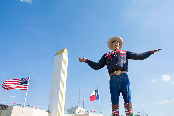 Big Tex at the Texas state fairgrounds Dallas, Texas USA - October 11, 2015: Big Tex standing in front of the texas state flag and the american state flag waving at the entrance of the texas state fair. Big tex is the symbol of the fair and has been an icon not only of the fair, but dallas city for many years.  large stock pictures, royalty-free photos & images