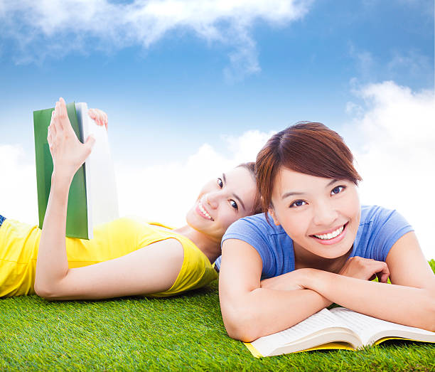 smiling pretty students lying on the grassland with books in the park